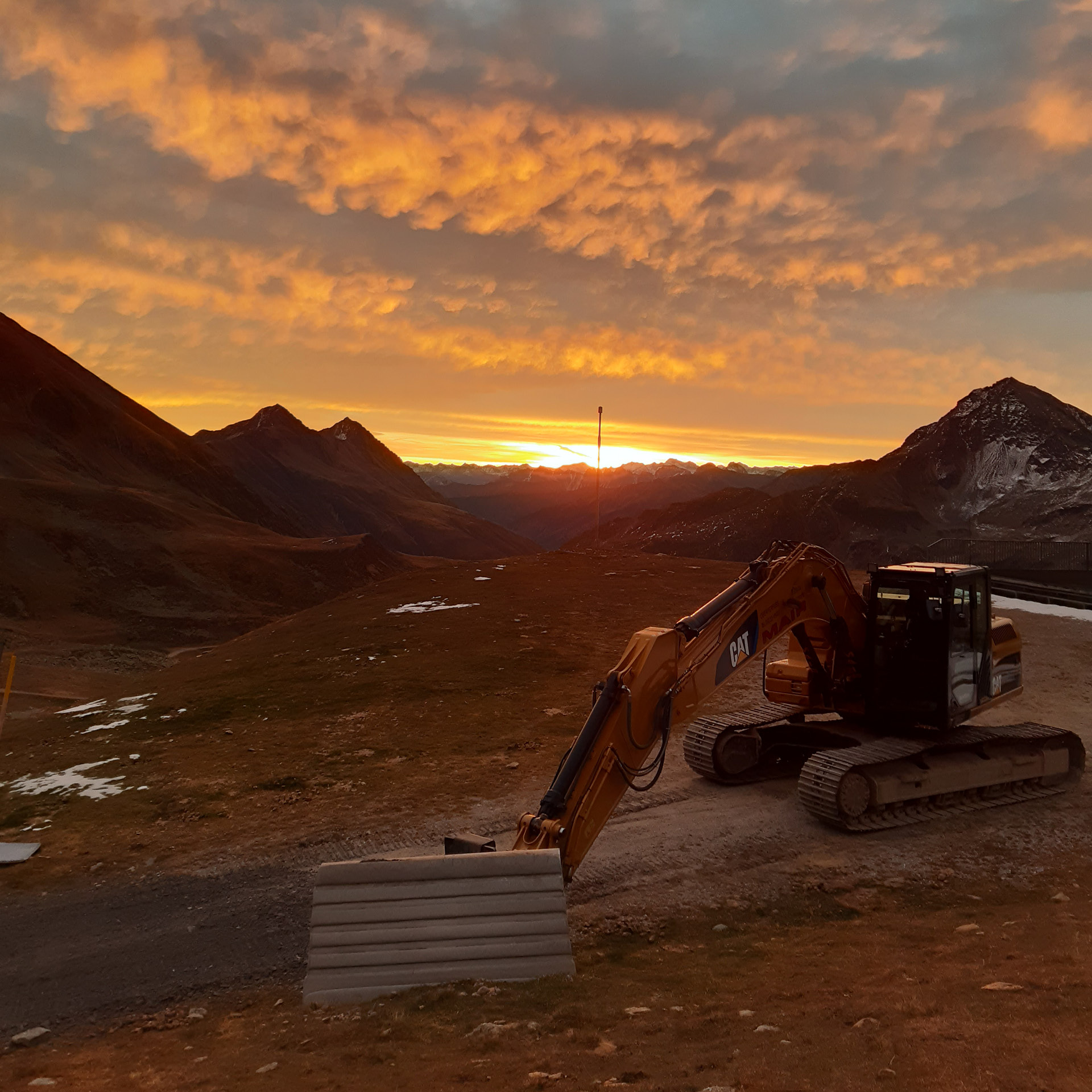 Kettenbagger beim Pisten- und Liftbau bei Sonnenuntergang