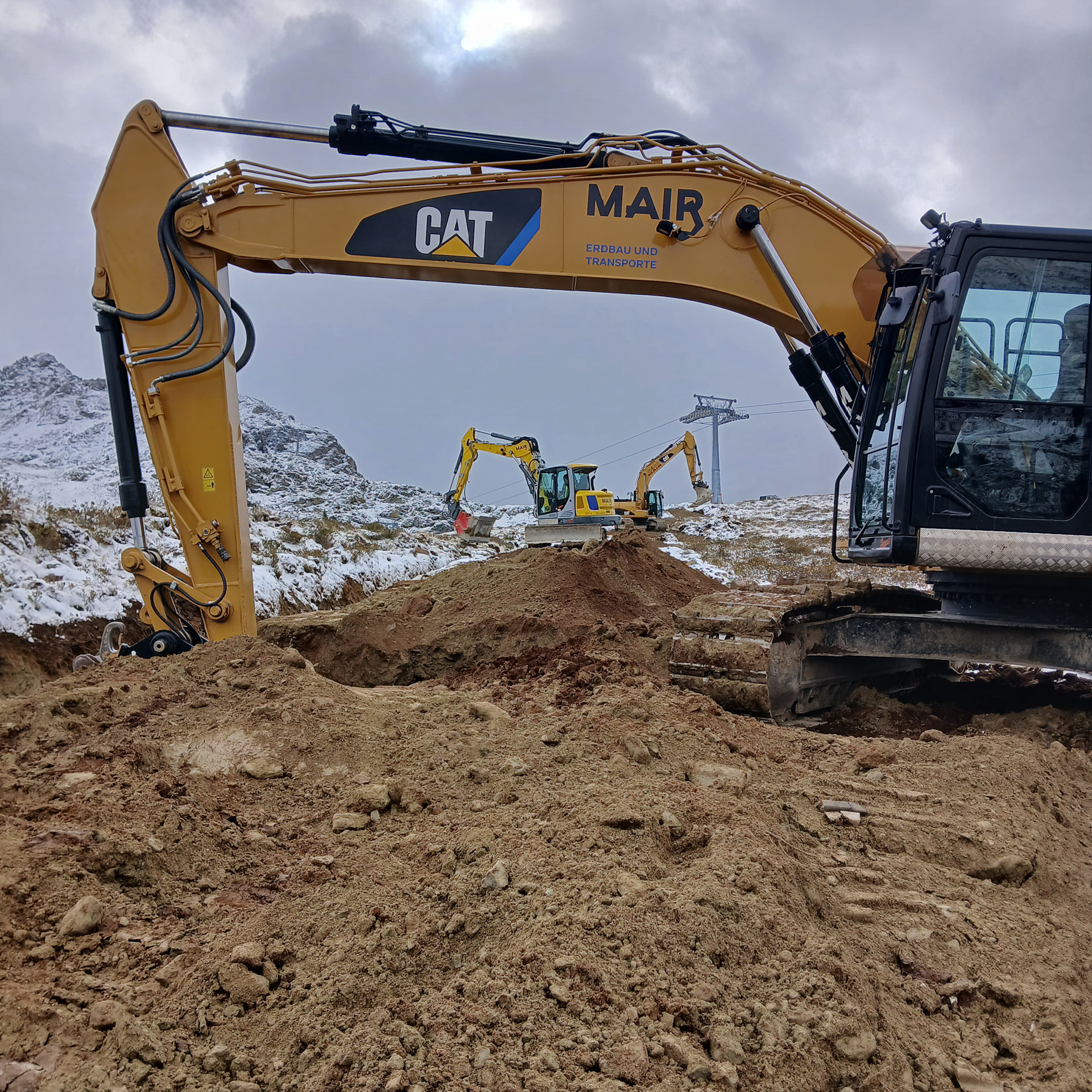 Mehrere Kettenbagger beim Pisten- und Liftbau bei Schnee