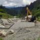 Kettenbagger transportiert einen großen Stein für die Wildbachverbauung, mehrere Wasserschleusen